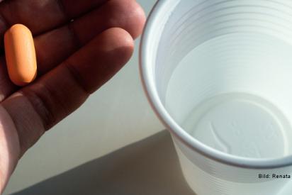 Hand mit einzelner Tablette darin, daneben ein Trinkbecher